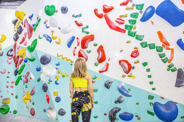 a blonde climber stands with her back against the background of a stone boulder