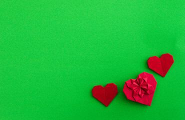 Red origami hearts on green background
