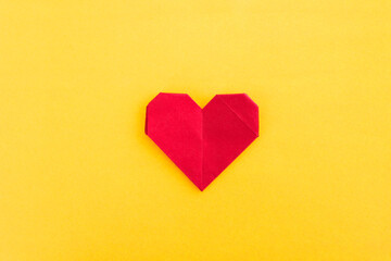 Red origami heart on yellow background