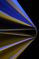 Papeles con doblez en forma de abanico con luz rasante azul y amarillo, forma un bello diseño abstracto con fondo negro