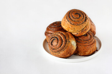 sweet twisted buns with poppy seeds on a plate on a white background.