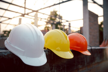 Safety helmet (hard hat) for engineer, safety officer, or architect, placed on cement floor with brick background. White, Yellow and Orange safety hat (helmet) in construction site.