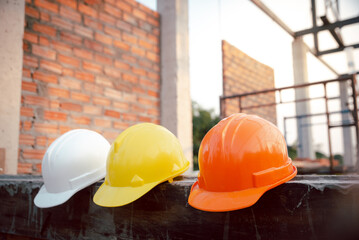 Safety helmet (hard hat) for engineer, safety officer, or architect, placed on cement floor with brick background. White, Yellow and Orange safety hat (helmet) in construction site. - obrazy, fototapety, plakaty