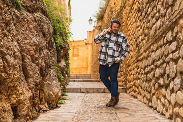 Fototapeta premium Chico con camisa cuadros blanca posando y tomándose fotos en callejón de piedra en pueblo blanco andaluz