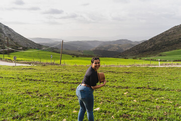 Chica joven guapa frente a paisaje montañoso  levantando los brazos y cogiendo sombrero en señal...