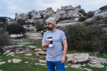 Chico bajito con sombrero de lana beige con vaso reutilizable de café en entorno natural montañoso