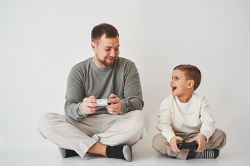 Fototapeta premium Emotional family playing console games on a white background. Father and son play gamepad games together.