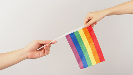 Two hands send and recive a rainbow flag on white background. LGBT CONCEPT.