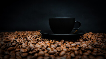 a  black cup of espresso on a black background and roasted coffee beans underneath. Coffee Background concept