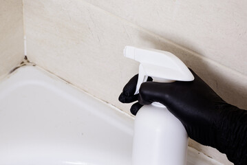 Dirty joints between the tiles, cleaning agent and hands in black gloves in the bathroom. Toxic...