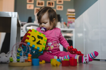 One small caucasian baby girl ten months old playing alone at home copy space using bricks and toys wearing pink on the floor in day