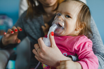 one baby and mother using nebulizer at home Woman hold her small girl child using vapor steam inhaler mask inhalation at home medical procedure medicament treatment asthma pneumonia bronchitis