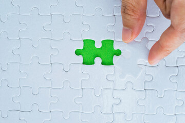 Hand putting the last piece of white jigsaw puzzle