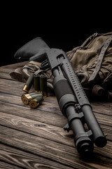 Obraz premium A black 12-gauge pump-action shotgun and ammo are on a canvas backpack. A smooth-bore weapon with a plastic stock. Dark background.