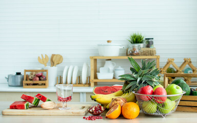 Background with nobody of fruits, pineapple, banana, pomegranate, red and green apples for good health decorated on wooden table in cozy white clean kitchen with copy space. Healthy food Concept.