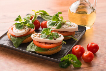 Caprese salad on bruschettas - sliced tomatoes, mozzarella, basil and topped with corn salad. Traditional Italian appetizer on black plate on wooden table background
