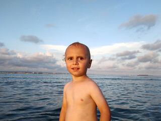 child bathes in the warm sea at sunset