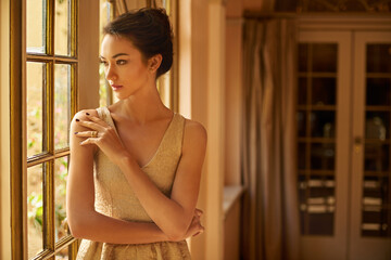 Perfect elegance. Shot of a beautiful and elegant young woman standing by a window.