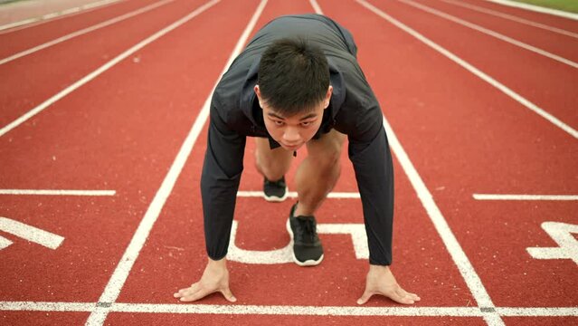 Young handsome chinese man doing star pose before running exercise on track in sport stadium. Challenge race of athletes running in the starting point.