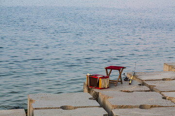 Alexandria, Egypt - January 2022: Fisherman's rod, a chair and a bag on the promenade without people. Minimalism