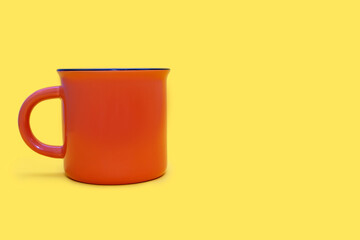 Orange mug on a yellow background with free space for text. Orange cup with a drink on a yellow background. Cafe or snack concept. Orange mug with the possibility of applying advertising or logo