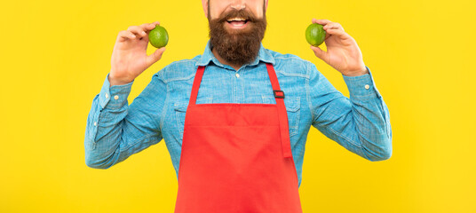 Happy man crop view in red apron holding fresh limes citrus fruits yellow background, fruiterer