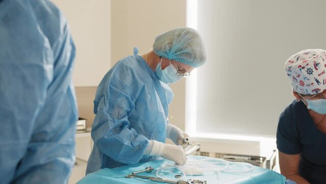 Scrub nurse preparing medical instruments for operation. Close-up Shot in Operating Room of Surgical Table with Instruments, Assistant Picks up Instruments for Surgeons During Operation