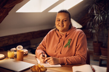 Fototapeta premium Young happy woman with mental health awareness ribbon studying at home and looking at camera.