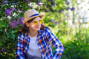 Girl in yellow sunglasses. Defocus beautiful young woman near blooming spring tree. Bush lilac flowers. Youth, love, fashion, romantic, lifestyle concept. Girl in hat nature background. Out of focus