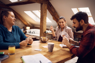 Group of happy friends having fun while playing cards at home.