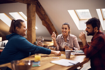 Young happy woman and her roommates playing poker with cards at college dorm.