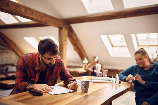 Male Student Writes Notes While Learning In Common Living Room.