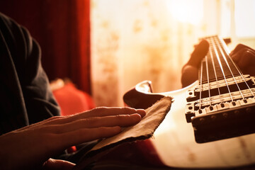 A young man wipes dust off an electric guitar. close-up. Sun rays.