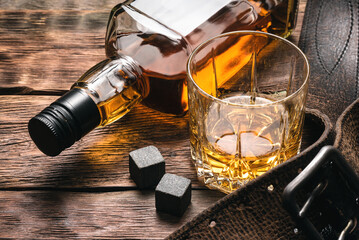 Whiskey in the drinking glass, bottle and leather wallet on the brown wooden table background