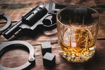 Whiskey in the drinking glass, gun and handcuffs on the detective desk concept background.
