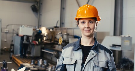 Portrait of a professional heavy industry engineer in uniform, goggles and a hard hat in a steel mill. Pretty industrialist woman standing at a metalwork facility.