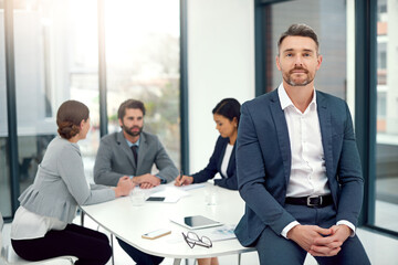 We all value each others expertise. Portrait of a businessman standing in a boardroom meeting with colleagues in the background.