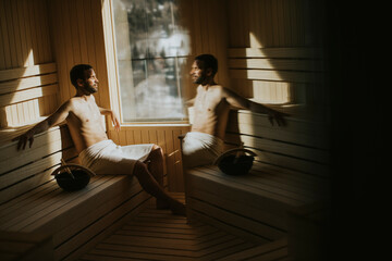 Young man relaxing in the sauna and watching winter forest through the window