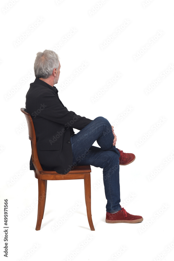 Wall mural side view of a man sitting  on chair with sneakers jeans and blazer looking background on white background