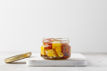 Open Glass Jar with Natural marinated greek feta cheese in jar with olive oil and herbs On board. Minimalistic