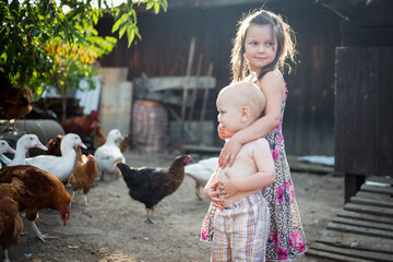 dzieci i zwierzęta - dziewczynka i chłopiec karmią kurki na wolnym wybiegu