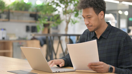 African American Man with Laptop Reading Documents 