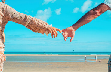Back view of man and woman hand to hand together in front of a tropical beach. Love and relationship couple people holding hands and enjoying leisure in summer holiday vacation. Blue Ocean and sky