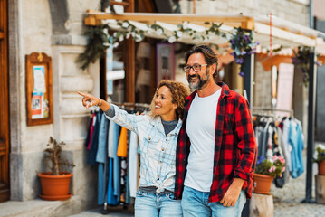 Fototapeta na wymiar Couple of happy young adult people enjoy shopping and tourist outdoor leisure activity in the street. Man and woman enjoy walking near stores smiling and pointing in friendship relationship love