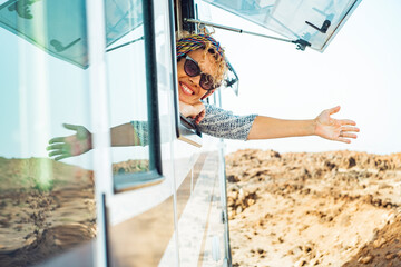 Cheerful happy tourist woman smile and do hallo gesture with hand outside the window of modern...