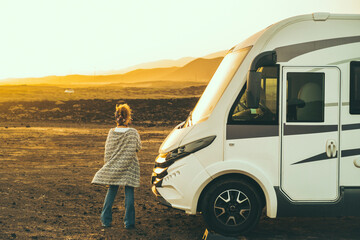 Concept of travel and freedom. Back view of standing woman admiring desert landscape near modern camper van motorhome. Alternative home lifestyle female people looking sunset free - Powered by Adobe