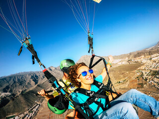 Happy tourist doing paragliding sport activity in outdoor leisure active lifestyle. Cheerful adult woman doing selfie picture flying on a paraglyde in summer holiday vacation. Freedom joyful people