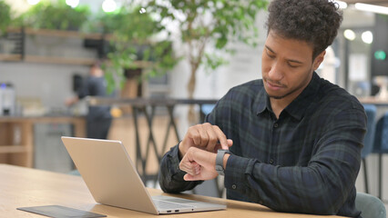 African American Man with Laptop Checking Smart Watch 