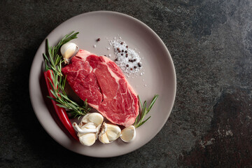 Raw beef steak with rosemary, garlic, salt, and pepper.