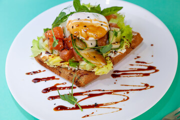 Toast with salmon and poached egg. Lettuce, cucumber, basil. A healthy breakfast sandwich. Microgreen and flax and sesame seeds. Wholesome food on a white plate. Fish with vegetables on bread.